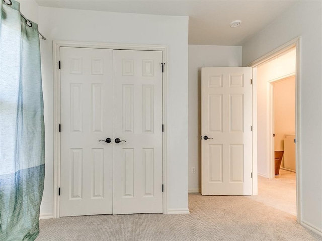 unfurnished bedroom featuring a closet, light colored carpet, and baseboards