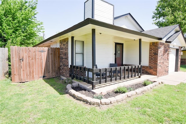 view of front of property featuring covered porch, fence, brick siding, a front lawn, and a garage