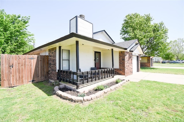view of side of property with a chimney, covered porch, an attached garage, a lawn, and brick siding
