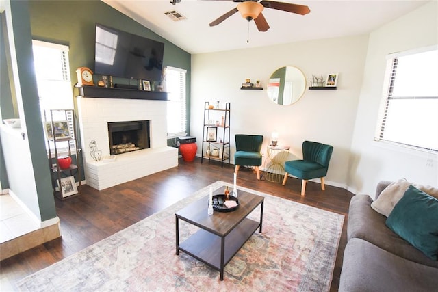 living room featuring wood finished floors, a brick fireplace, baseboards, visible vents, and a ceiling fan