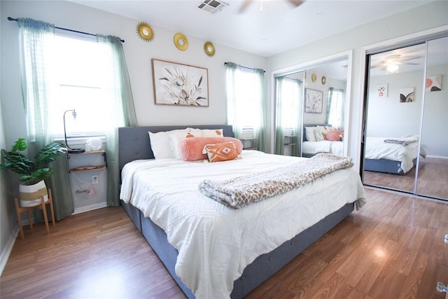 bedroom featuring ceiling fan, multiple closets, visible vents, baseboards, and wood finished floors