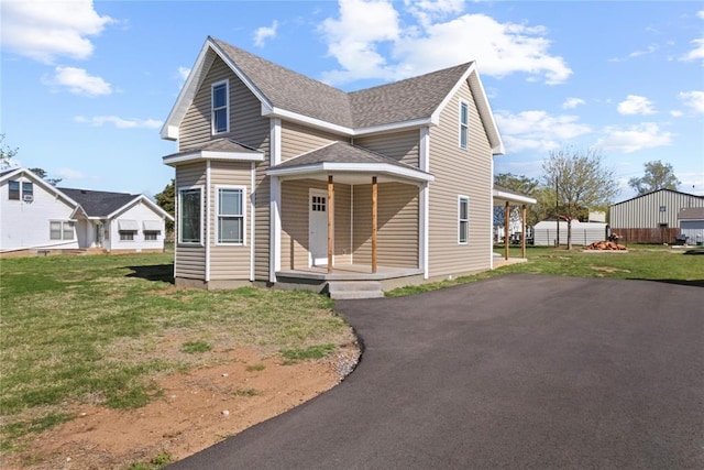 traditional-style home with a front lawn, driveway, a shingled roof, and covered porch