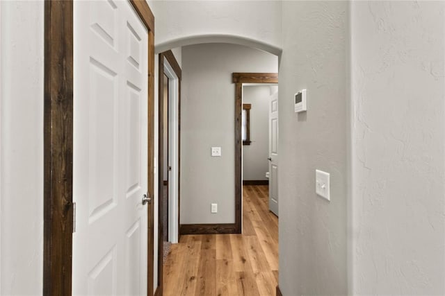 hallway featuring arched walkways, light wood-style floors, and baseboards