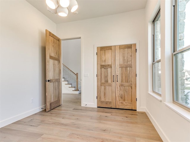 unfurnished room with an inviting chandelier, light wood-type flooring, stairs, and baseboards