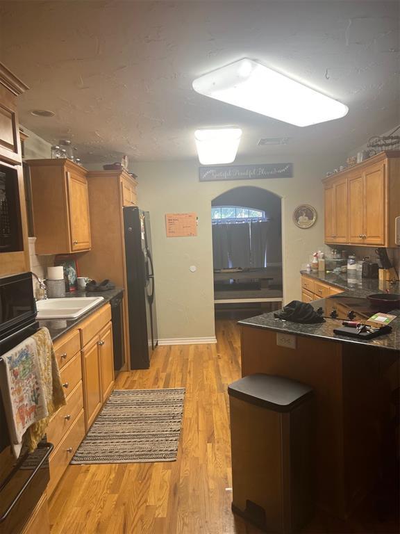501 S 7th St, Okemah, OK 74859 - kitchen featuring dark countertops, a sink, black appliances, a peninsula, and light wood-style flooring