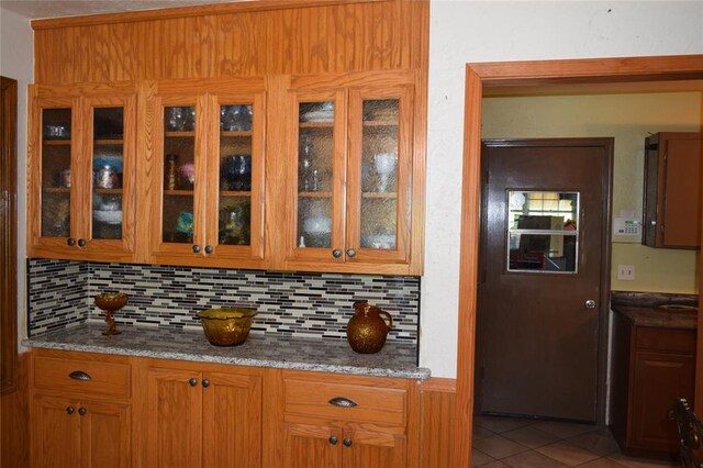 1400 S Indian Meridian Rd, Choctaw, OK 73020 - interior space with dark stone counters, tile patterned floors, brown cabinets, glass insert cabinets, and backsplash