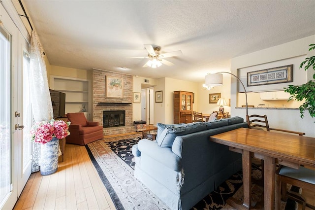 living area featuring a ceiling fan, a textured ceiling, built in features, a fireplace, and light wood finished floors