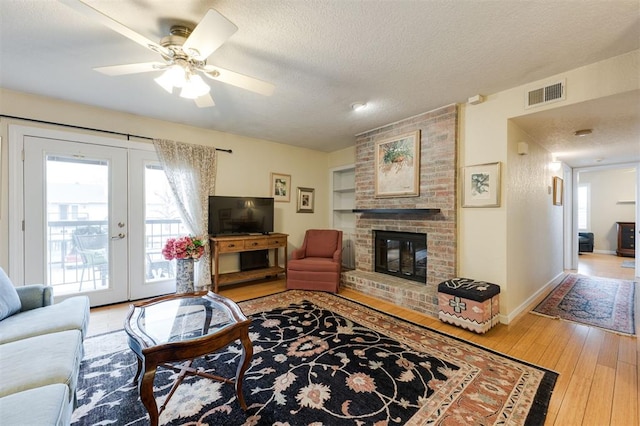 3200 W Britton Rd Unit 232, Oklahoma City, OK 73120 - living area featuring light wood-style flooring, a textured ceiling, a brick fireplace, ceiling fan, and french doors