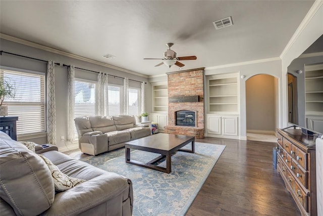 living room with visible vents, a ceiling fan, baseboards, a brick fireplace, and built in shelves