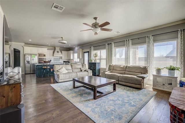living room featuring dark wood-style flooring, visible vents, crown molding, and a ceiling fan