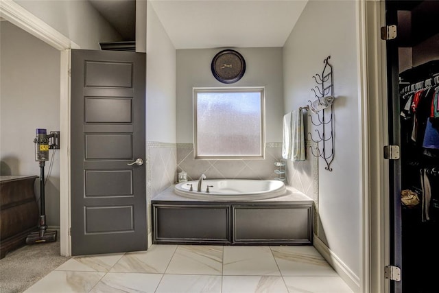 bathroom featuring a spacious closet, a garden tub, and marble finish floor