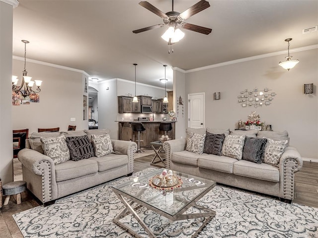 living area with wood finished floors, visible vents, ornamental molding, baseboards, and ceiling fan with notable chandelier