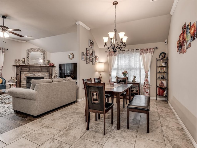 dining space featuring ceiling fan with notable chandelier, vaulted ceiling, baseboards, and a fireplace