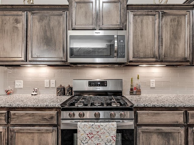 kitchen with dark brown cabinets, appliances with stainless steel finishes, tasteful backsplash, and light stone counters