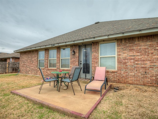 back of property featuring fence, brick siding, a patio area, a shingled roof, and a yard
