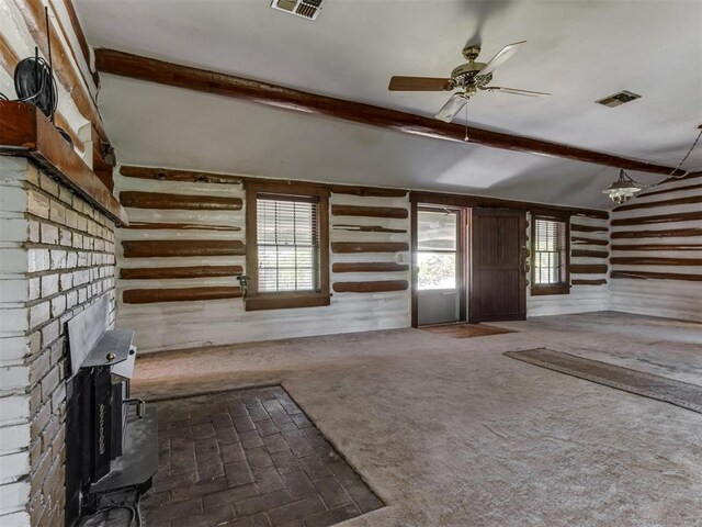 unfurnished living room with visible vents, wood walls, a brick fireplace, vaulted ceiling with beams, and a ceiling fan