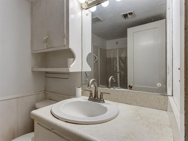 bathroom with vanity, a wainscoted wall, toilet, and visible vents