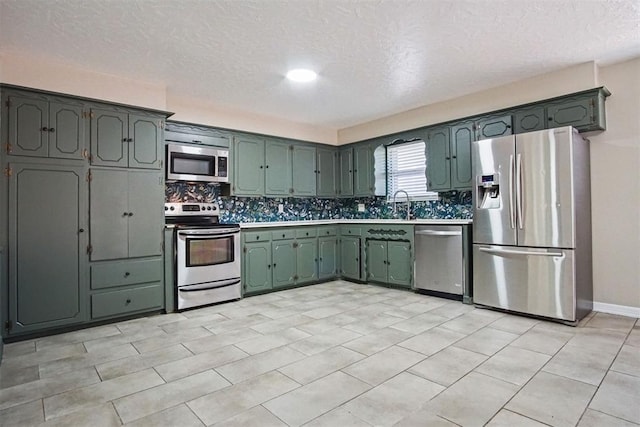 kitchen featuring tasteful backsplash, a sink, a textured ceiling, light countertops, and appliances with stainless steel finishes