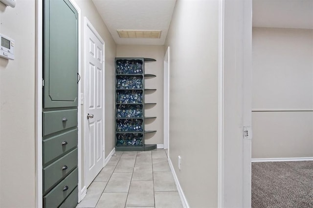 corridor featuring baseboards, visible vents, and light tile patterned flooring