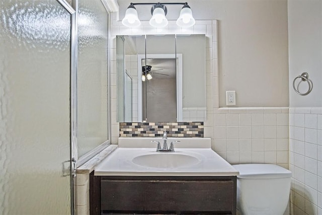 full bath with a shower stall, vanity, tile walls, ceiling fan, and toilet