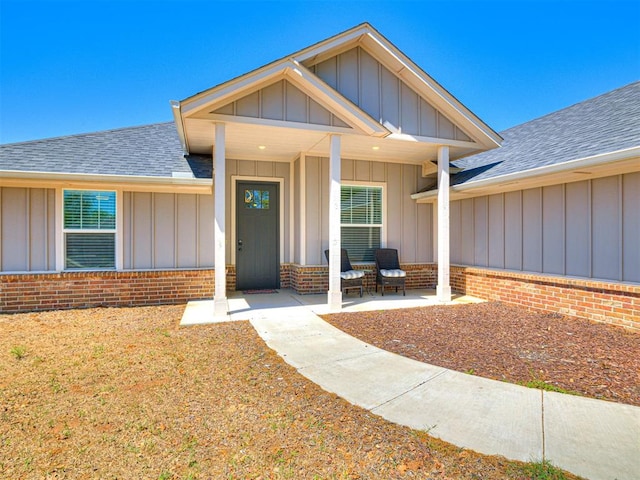 property entrance featuring board and batten siding, roof with shingles, a porch, and brick siding