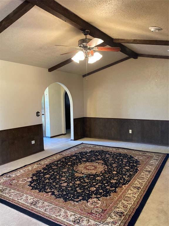 unfurnished room with ceiling fan, a wainscoted wall, arched walkways, carpet floors, and a textured ceiling