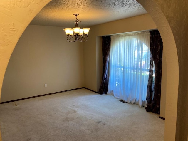 empty room featuring carpet floors, a chandelier, a textured ceiling, arched walkways, and baseboards