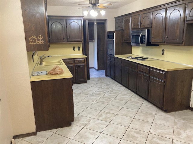 kitchen with a sink, appliances with stainless steel finishes, dark brown cabinets, light tile patterned flooring, and a textured ceiling