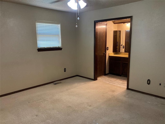 unfurnished bedroom with light colored carpet, baseboards, connected bathroom, ceiling fan, and a textured ceiling