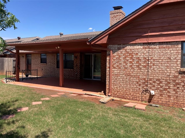 back of property with a patio, brick siding, a chimney, and roof with shingles