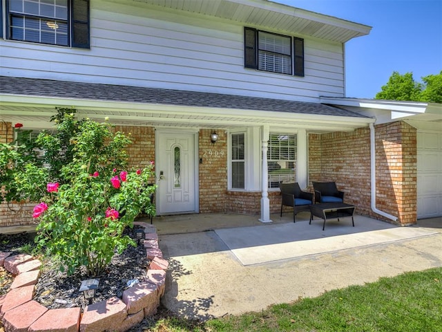 2909 Wheeler Ct, Oklahoma City, OK 73127 - property entrance featuring a garage, brick siding, roof with shingles, and covered porch