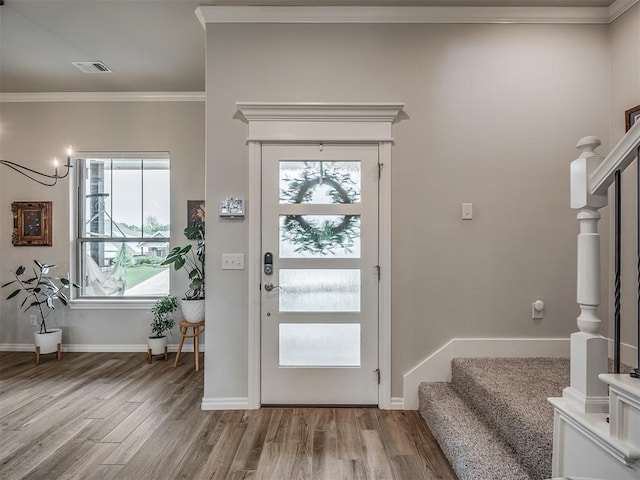 doorway with visible vents, wood finished floors, baseboards, ornamental molding, and stairs