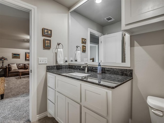 half bathroom with vanity, baseboards, toilet, and visible vents