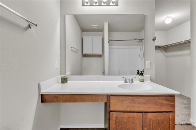 full bath with wood finished floors, a walk in closet, a shower, and vanity