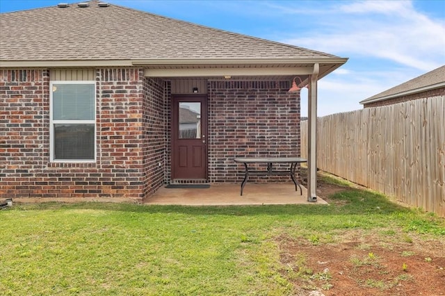 property entrance featuring brick siding, fence, a lawn, and roof with shingles