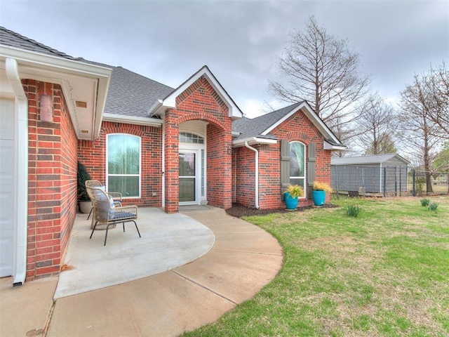 exterior space featuring a lawn, roof with shingles, brick siding, and a patio area