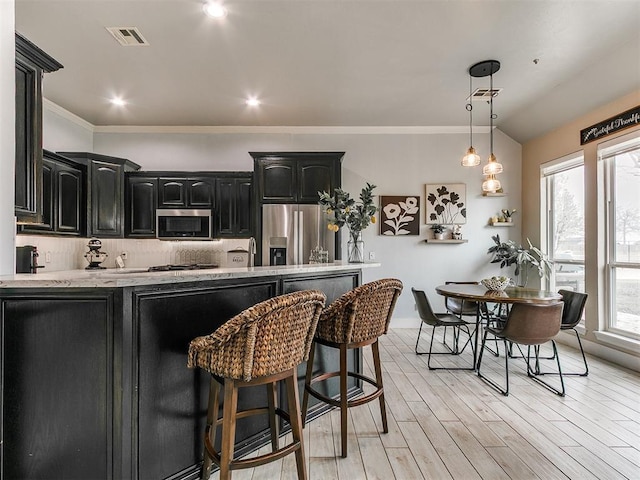 kitchen with light wood finished floors, stainless steel appliances, a kitchen breakfast bar, visible vents, and dark cabinetry