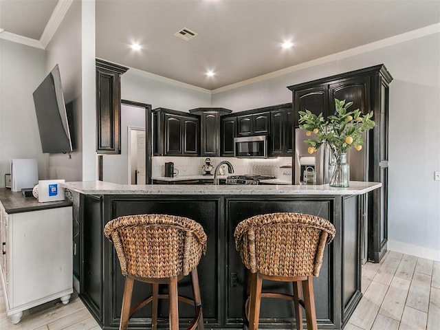 kitchen with dark cabinetry, light wood-style flooring, light stone countertops, and stainless steel microwave