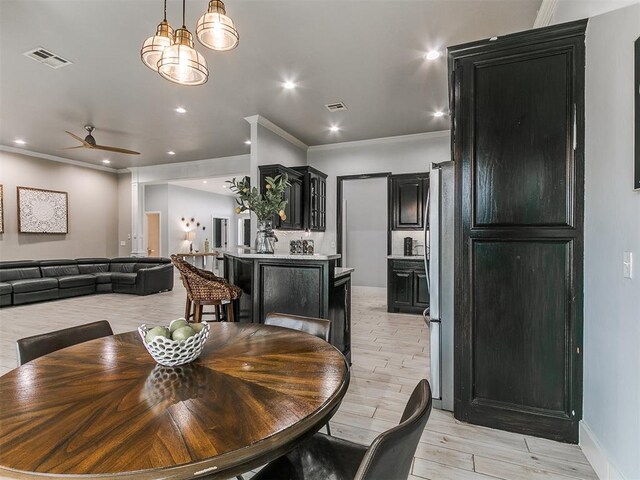 dining area featuring light wood finished floors, baseboards, visible vents, a ceiling fan, and ornamental molding
