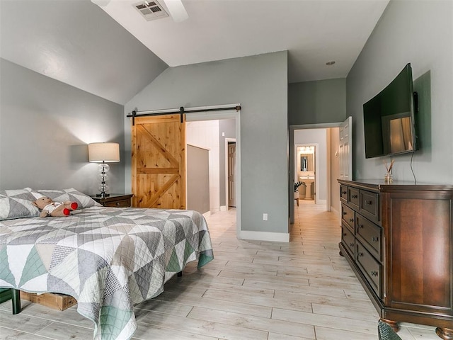 bedroom with a barn door, vaulted ceiling, visible vents, and light wood-style flooring
