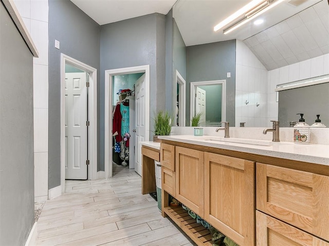 full bathroom featuring wood finished floors, a spacious closet, vanity, baseboards, and lofted ceiling