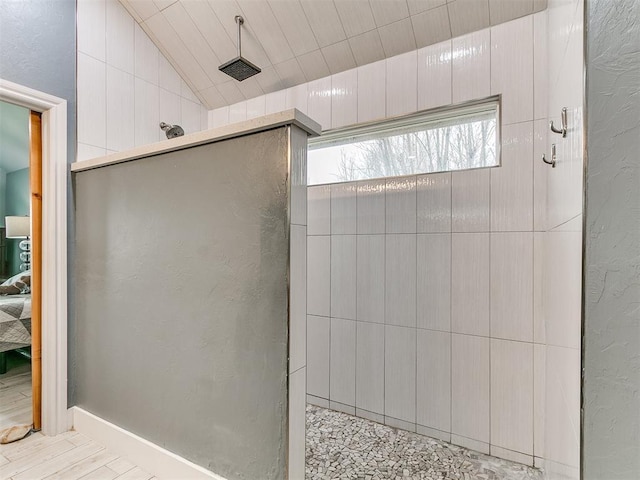 bathroom with vaulted ceiling, a textured wall, wood finished floors, and a walk in shower