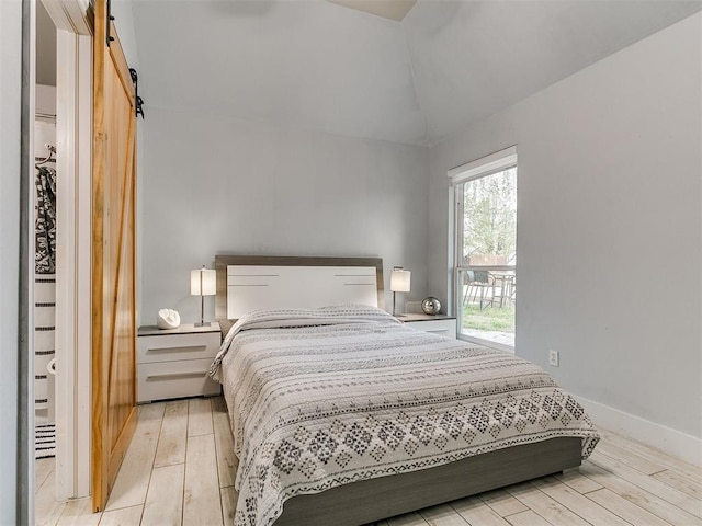 bedroom featuring light wood finished floors, vaulted ceiling, baseboards, and a barn door