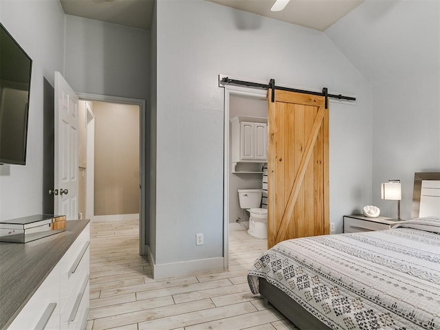 bedroom with a barn door, lofted ceiling, baseboards, light wood-style flooring, and ensuite bathroom