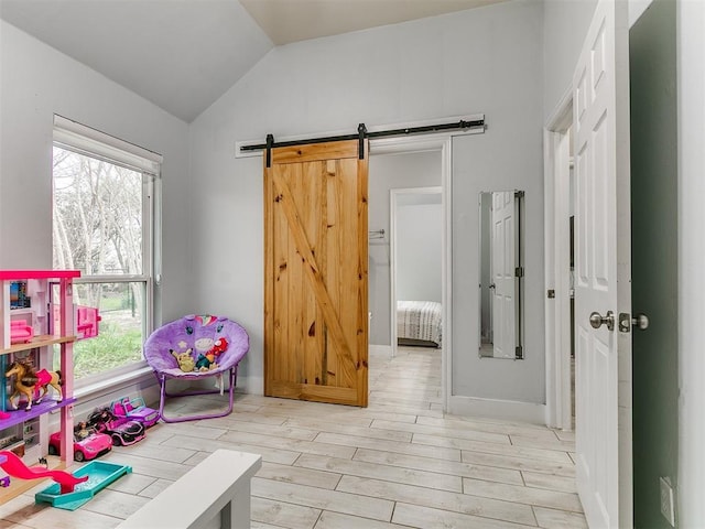 playroom with vaulted ceiling, a healthy amount of sunlight, light wood-style floors, and a barn door