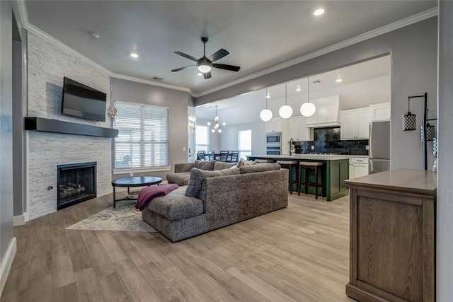 4145 Thunderhead Rd, Norman, OK 73072 - living room featuring a ceiling fan, light wood-type flooring, a stone fireplace, a chandelier, and ornamental molding