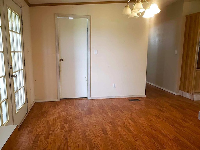 empty room with an inviting chandelier, baseboards, wood finished floors, and visible vents