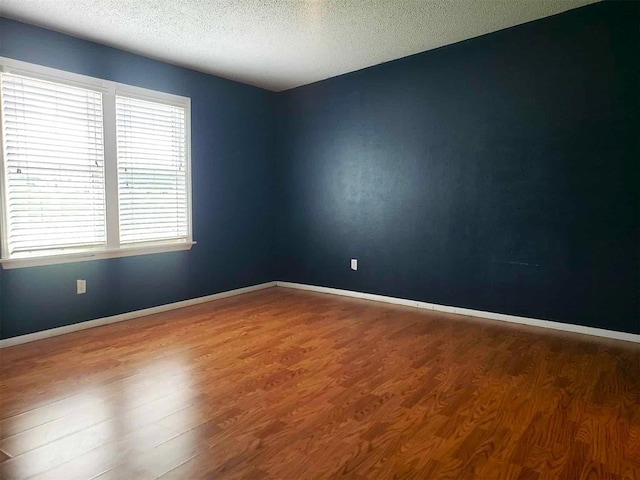 spare room featuring baseboards, a textured ceiling, and wood finished floors