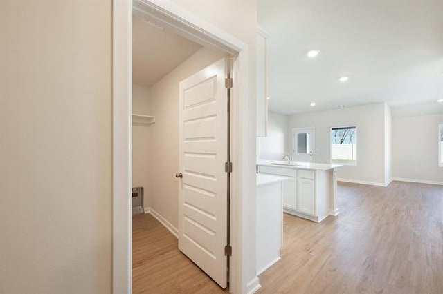 corridor featuring recessed lighting, baseboards, a sink, and light wood-type flooring