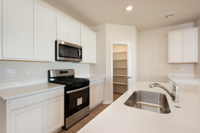 kitchen featuring light wood finished floors, stainless steel appliances, light countertops, visible vents, and a sink